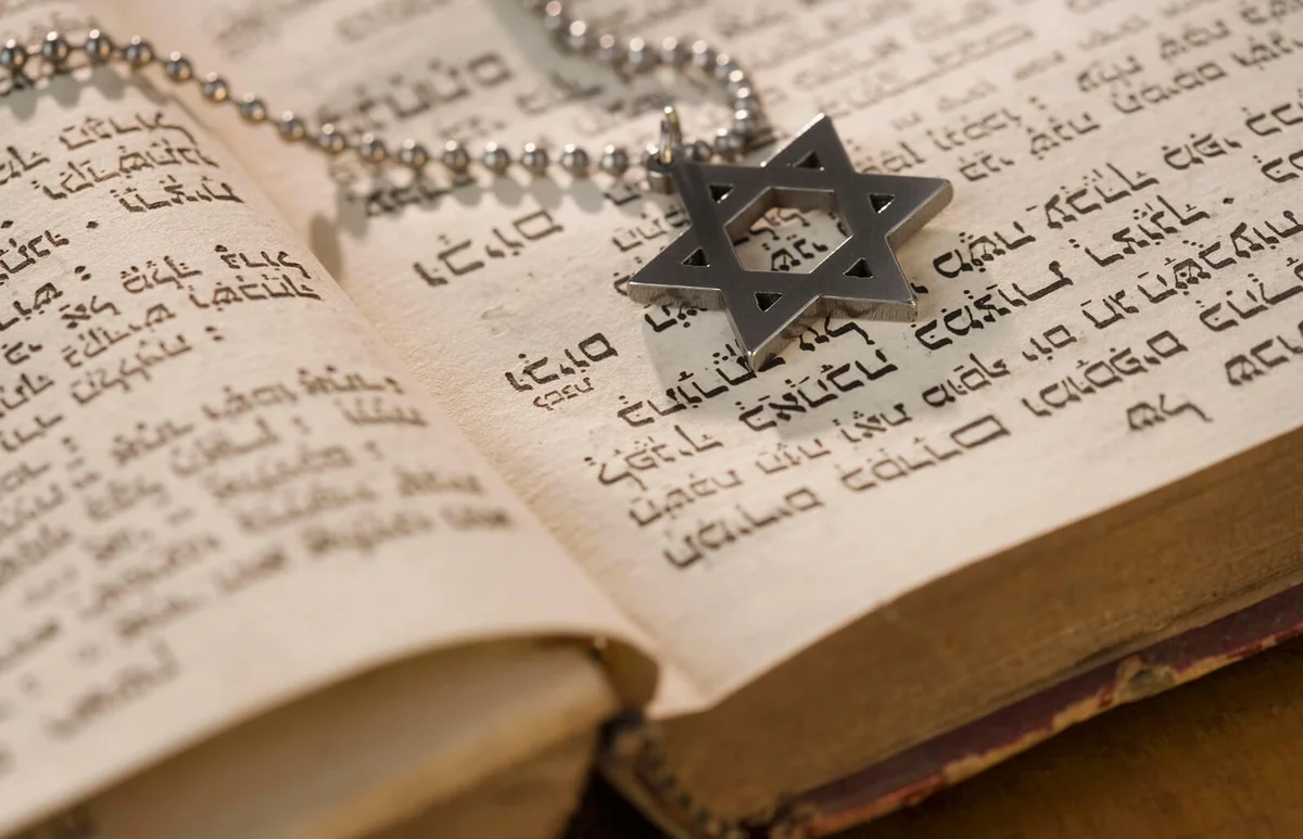Star of David necklace on book with Hebrew text