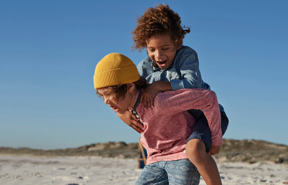 Kids smiling & piggy backing on beach by the ocean