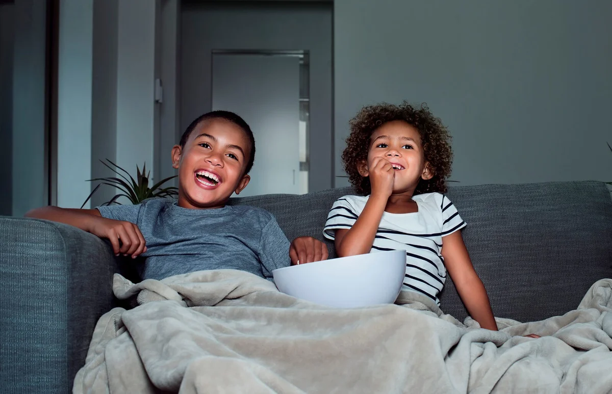 Happy siblings having popcorn while watching TV