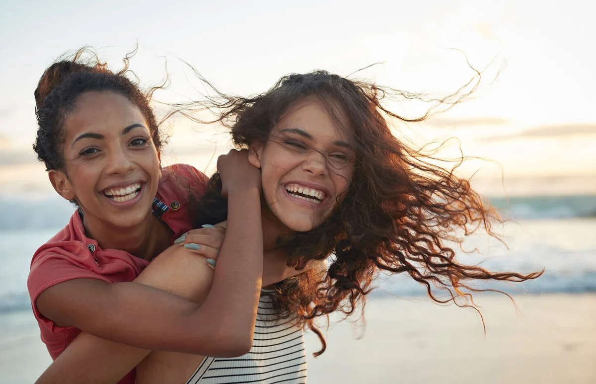 Young women piggybacking on sandy beach