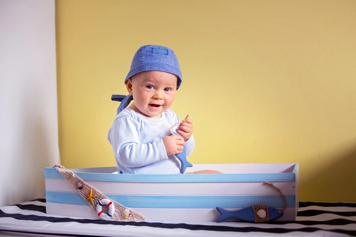 Cute toddler boy, sitting in a big wooden boat at home