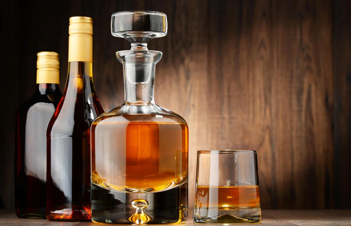 Bottles of assorted alcoholic beverages and glass of whisky