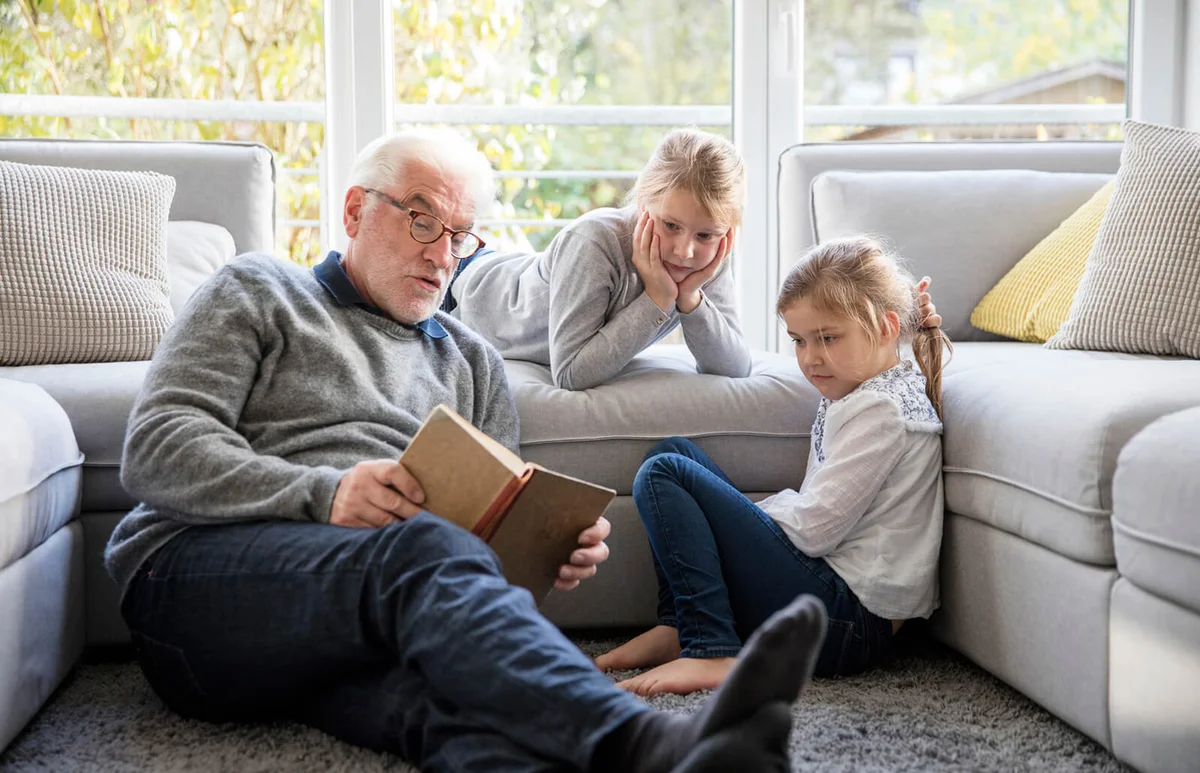 Two girls and grandfather reading book in living room