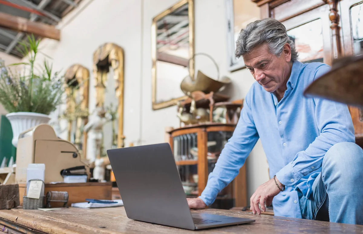 man looking at computer in his antique shop