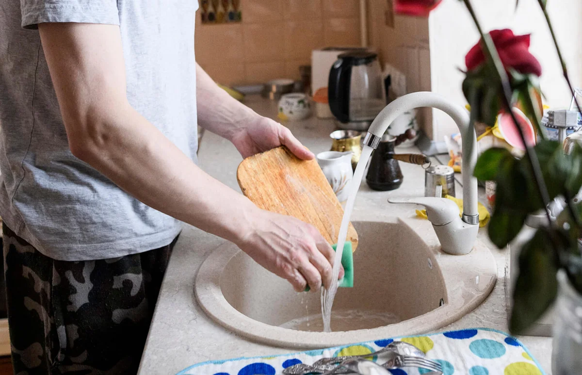 Mid adult man washing cutting board in kitchen sink at home