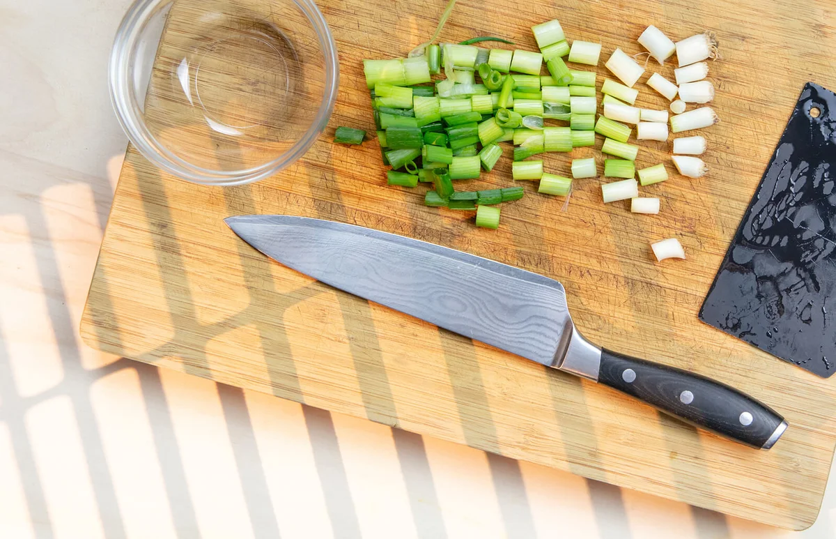 kitchen scraper and kitchen knife on bamboo cutting board