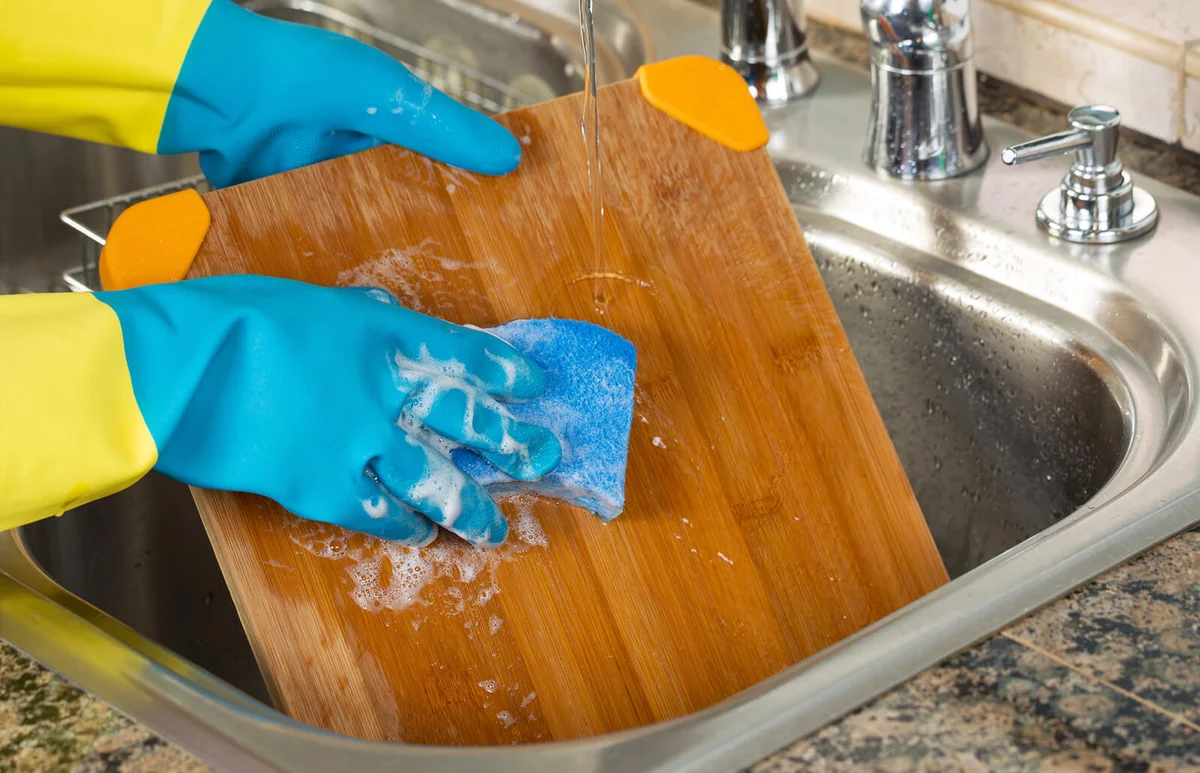 Cleaning Wooden Cutting board inside of Kitchen Sink with sponge