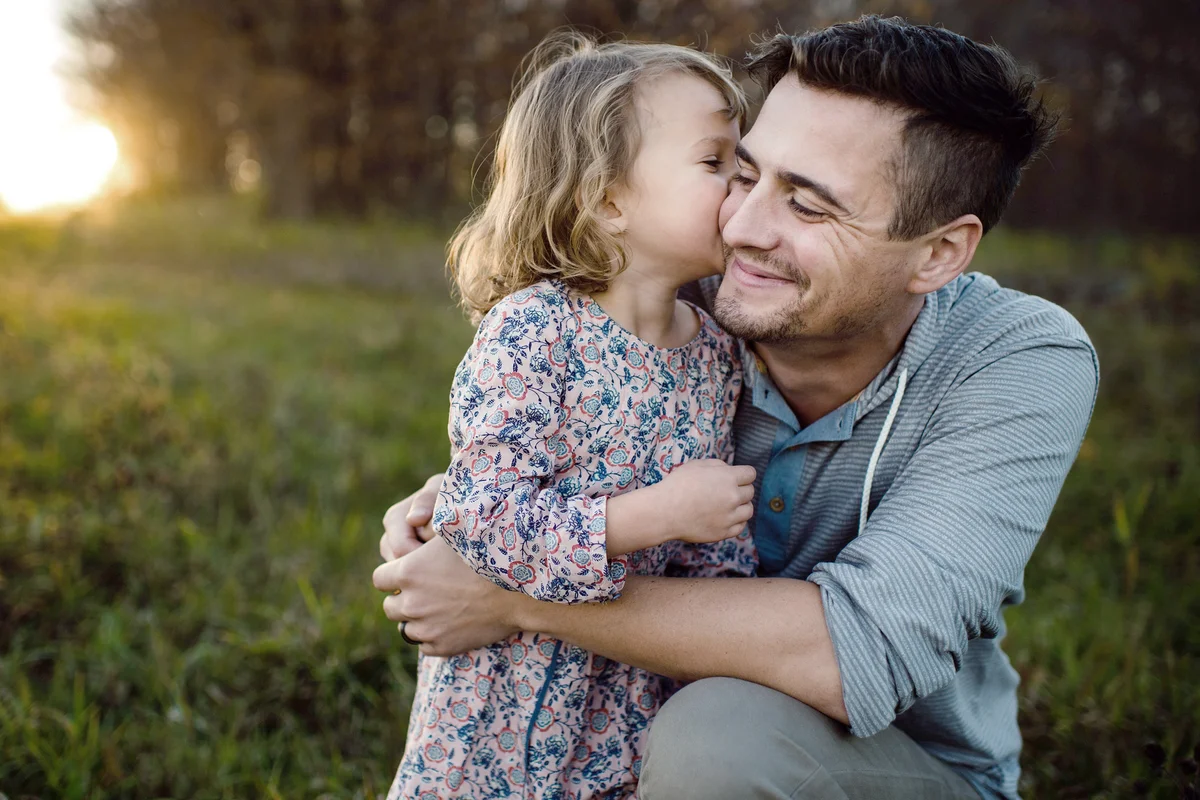 Girl kissing father on cheek in field