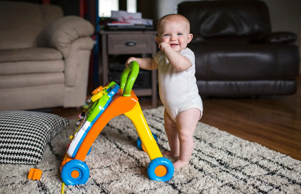 Portrait of happy baby girl with walker standing on rug at home