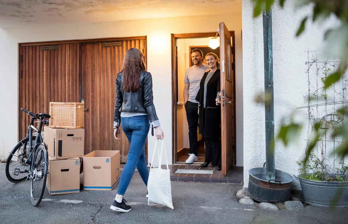 Parents looking at daughter walking by cardboard boxes and bicycle outside house