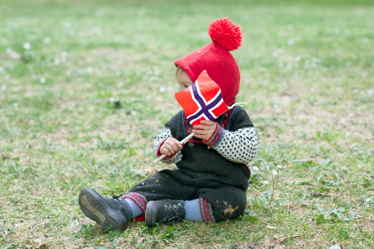 Child sitting on grass holding Norwegian flag