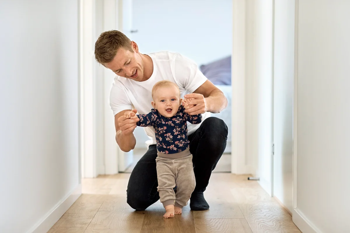 Man teaching little son to walk in corridor