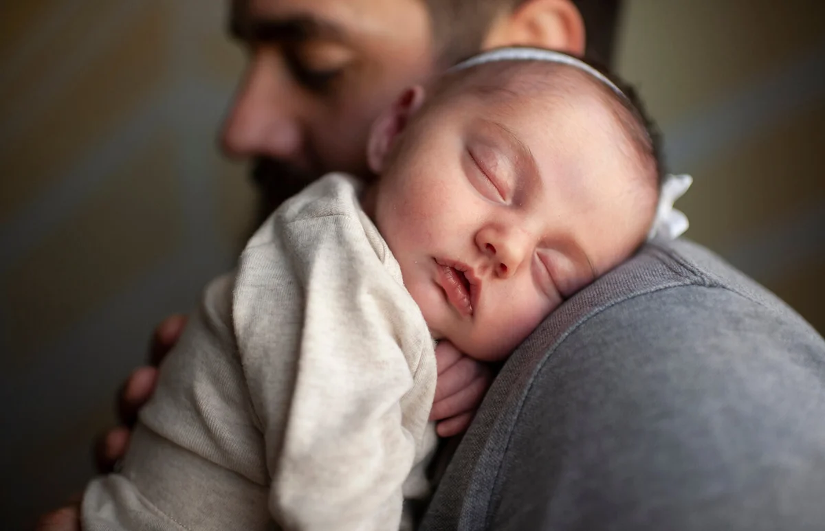 newborn baby's face sleeping on father's shoulder at home