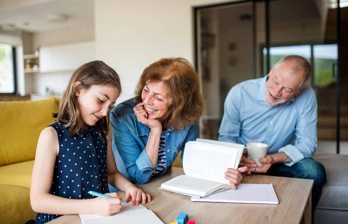Senior grandparents and granddaughter sitting indoor at the table