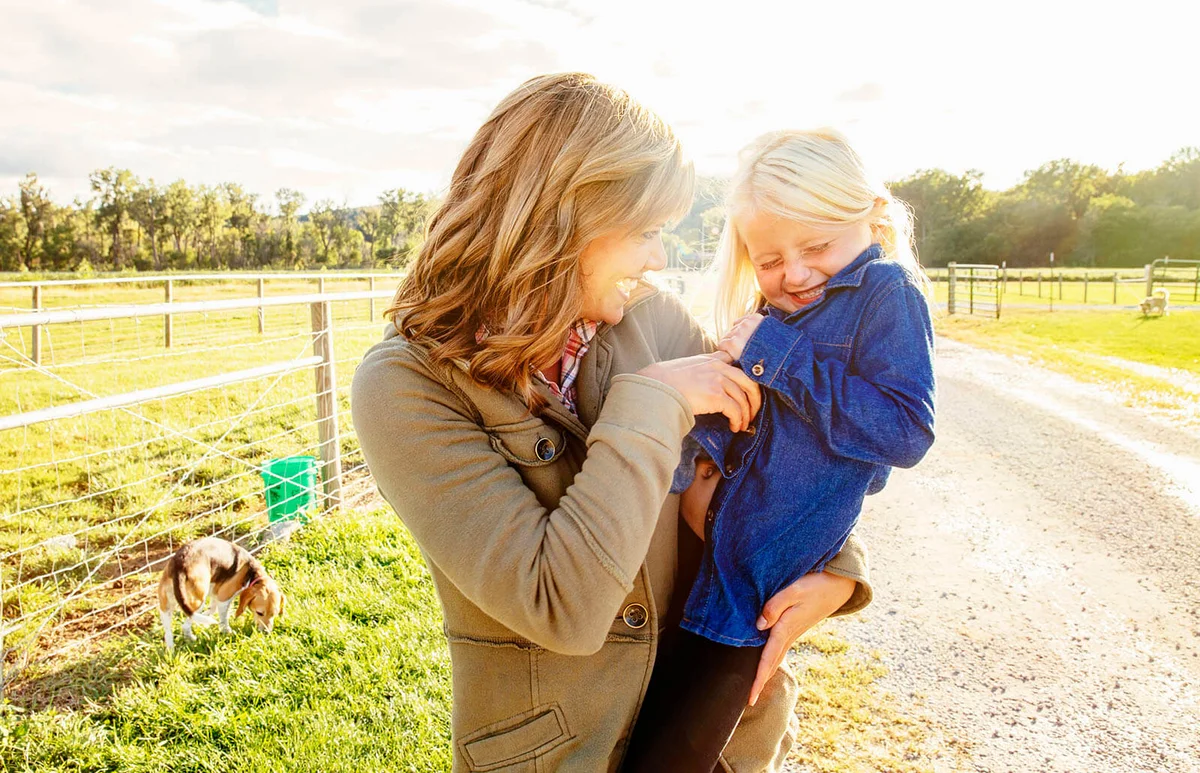 mother tickling daughter on rural road