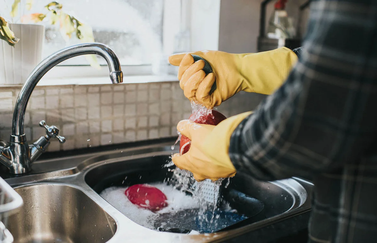 Man standing at the sink, wearing yellow marigold gloves, washing the dishes