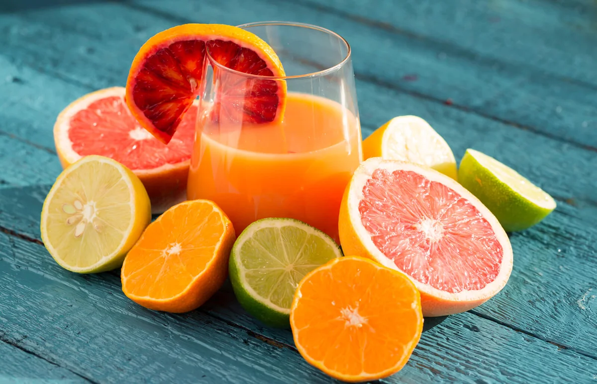 Halved citrus fruits (tangerine, lemone, lime, blood orange) arranged around a glass of juice