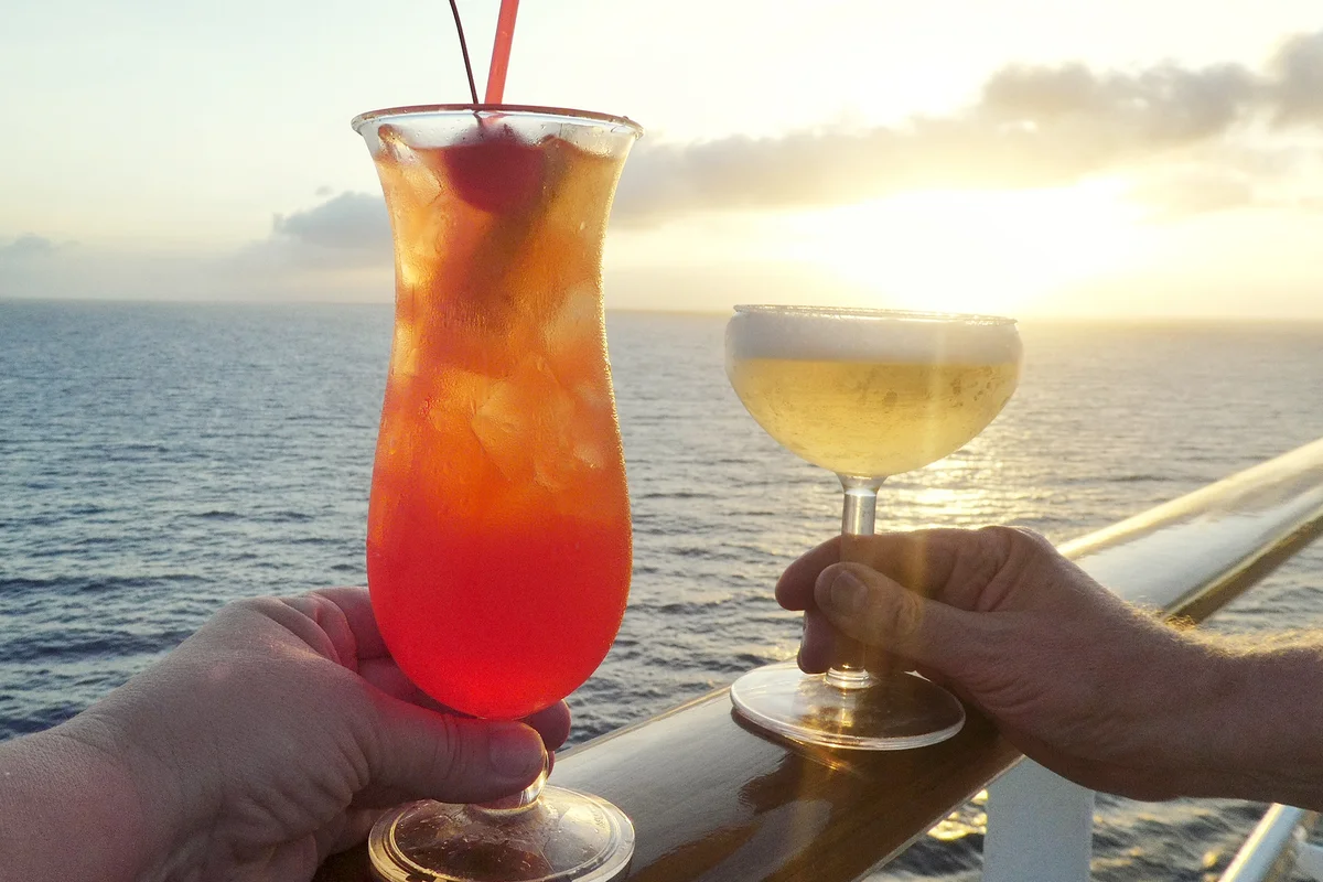 Hands Holding Cocktails Against Sea At Sunset