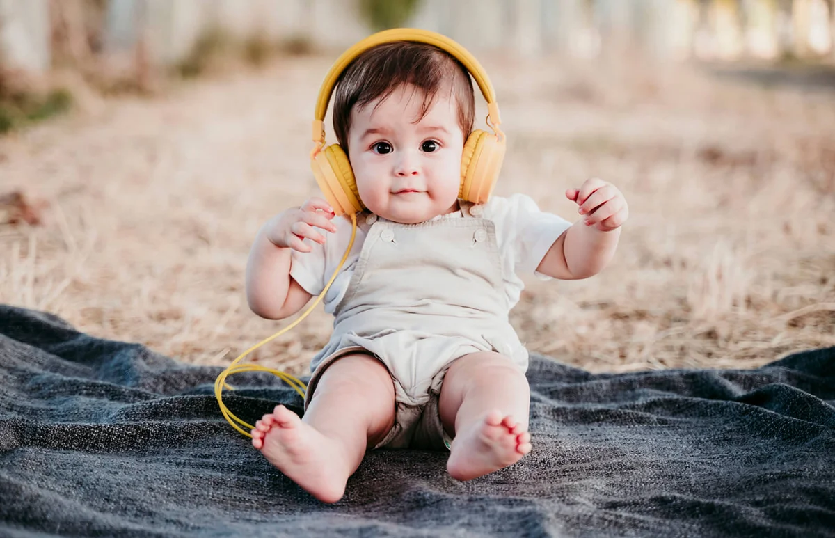 Cute baby boy wearing headphones while sitting on blanket outdoors