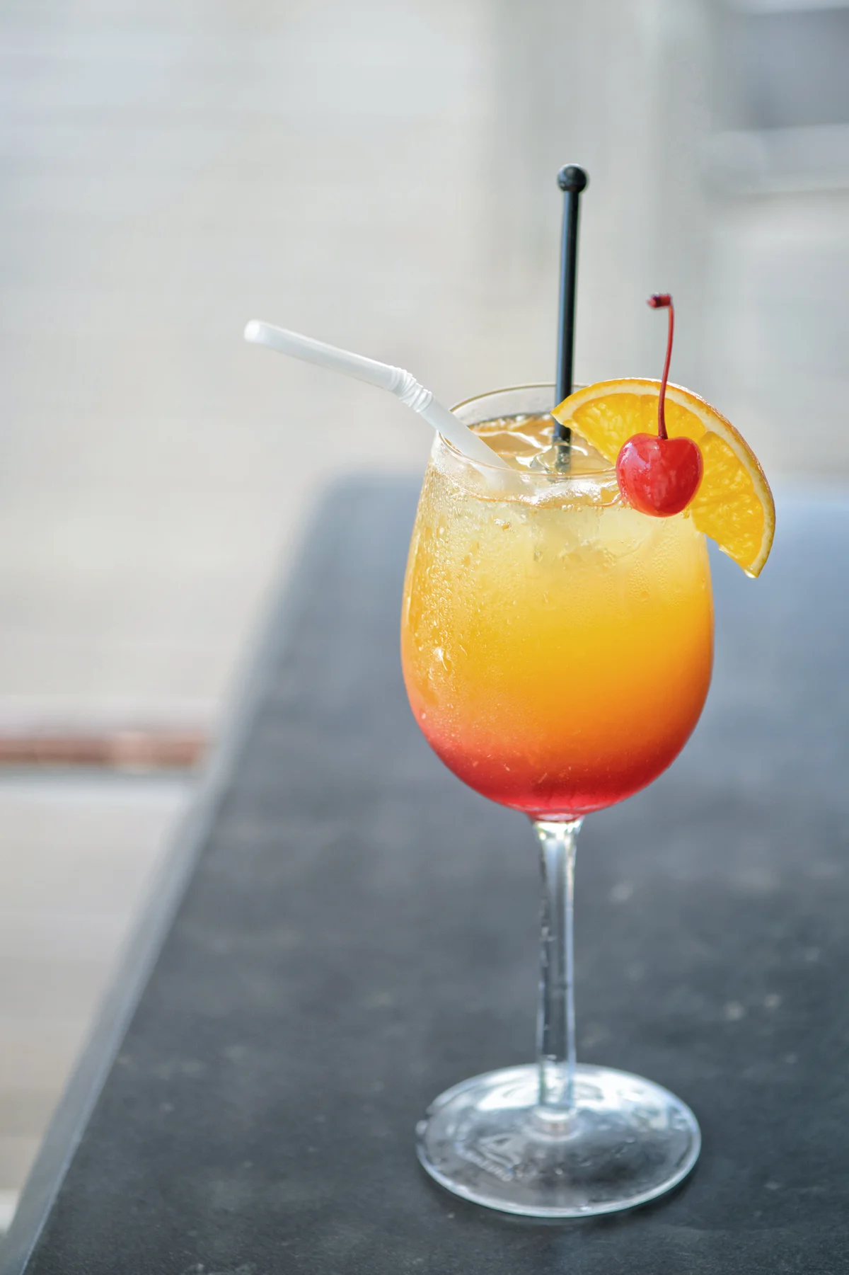 Red cocktail with an orange slice and cherry on the background of the a table