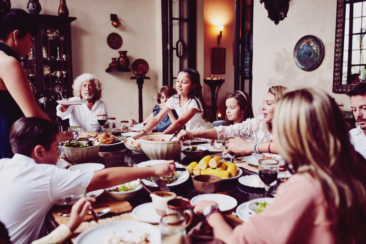 Young girl bringing platter of bread to dining room table during family meal