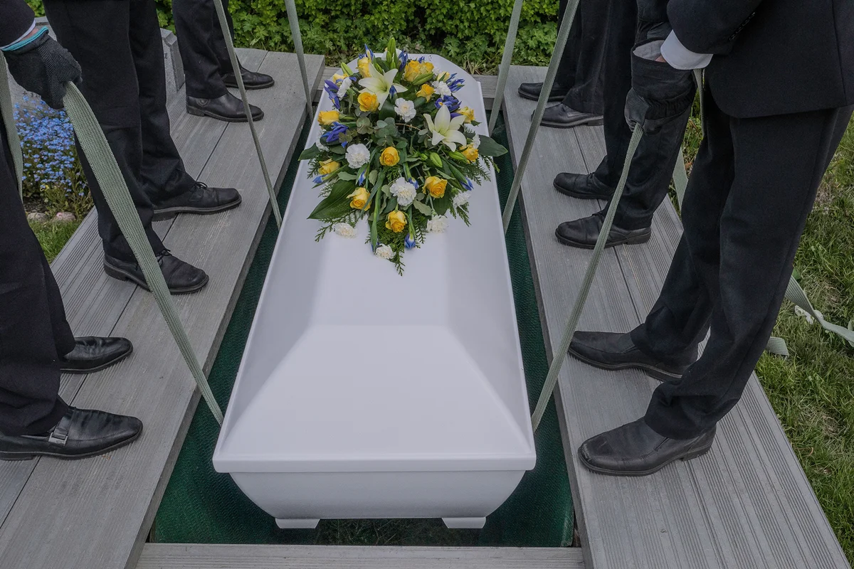 A coffin is lowered by six men into the grave