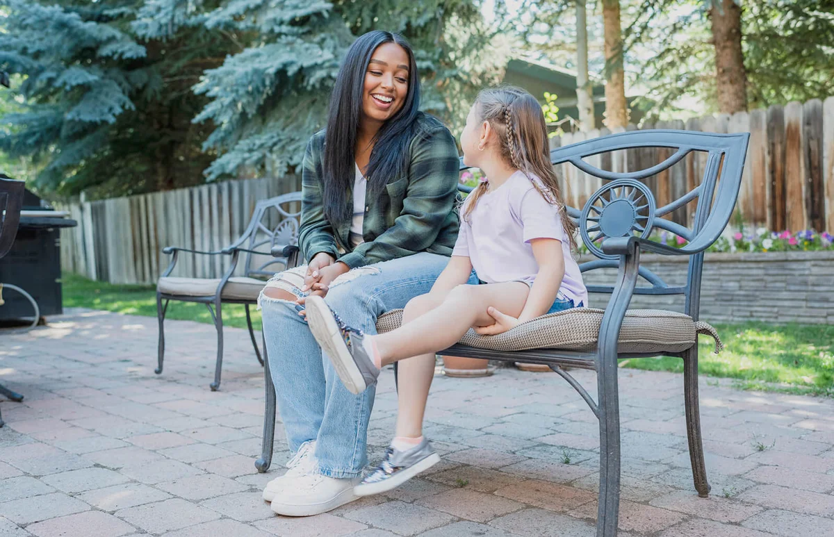 Young woman and small girl sitting on bench in back yard