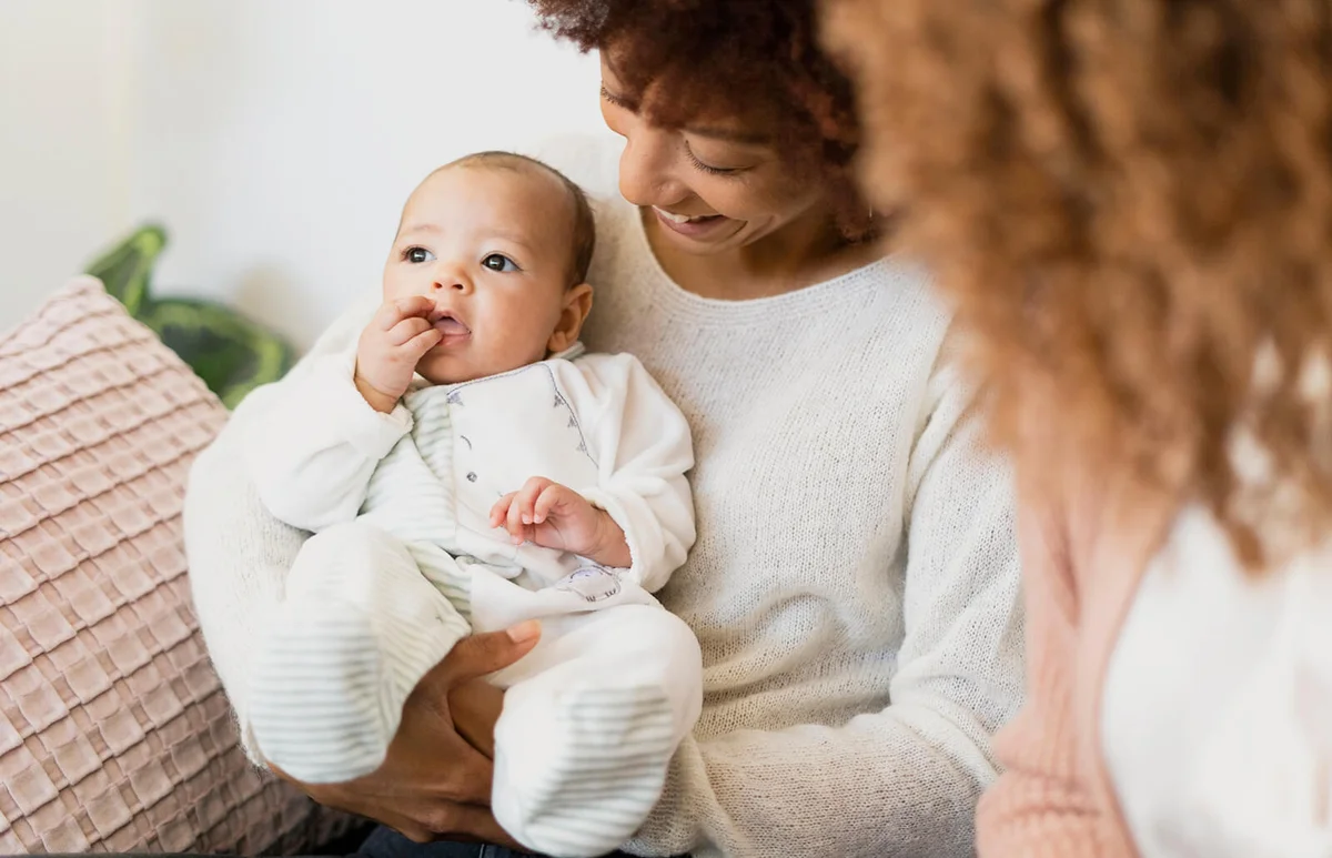 Aunt holding niece while mother sitting beside at home