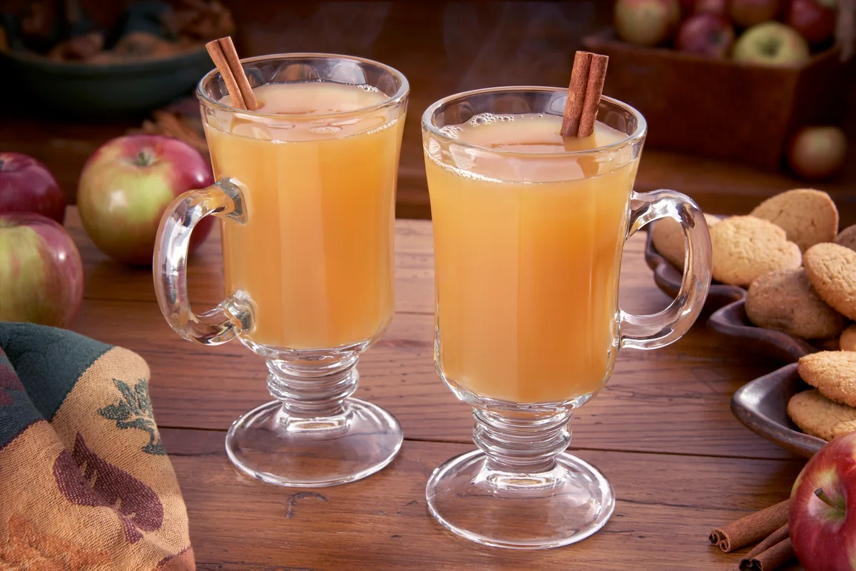 Steaming hot apple cider on a table with apples and ginger cookies