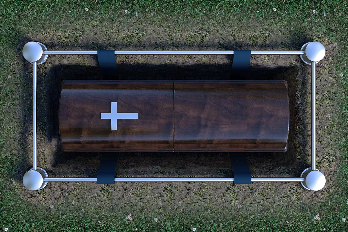 A modern wooden coffin at a funeral being lowered into a grave