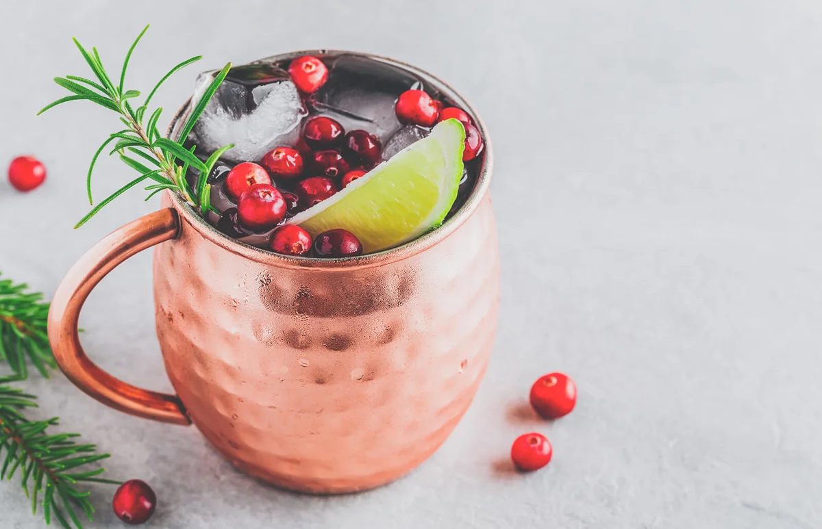 Holiday Moscow Mule ice cold Cocktail in copper cup with cranberries, lime and rosemary