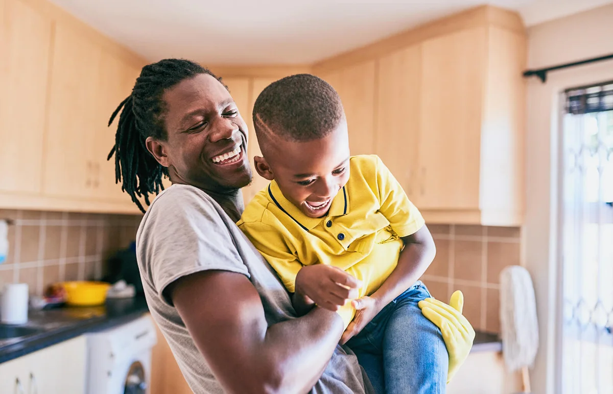 affectionate young single father playing with his son while cleaning in their kitchen at home