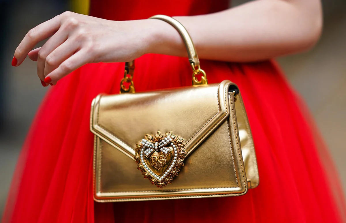 A guest wears a shiny gold color Dolce & Gabbana handbag, outside the Dolce & Gabbana show during Milan Fashion Week Spring/Summer 2020 on September 22, 2019 in Milan, Italy | Getty Editorial Use