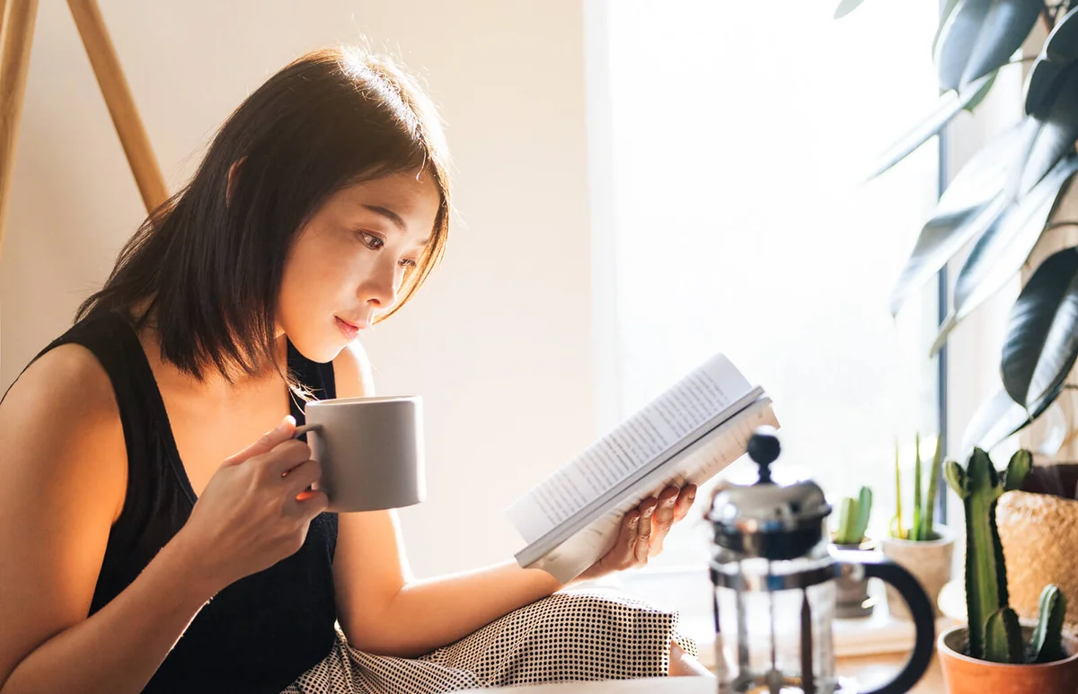 young woman reading a book while drinking coffee