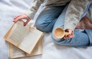 Woman in bed with coffee and book