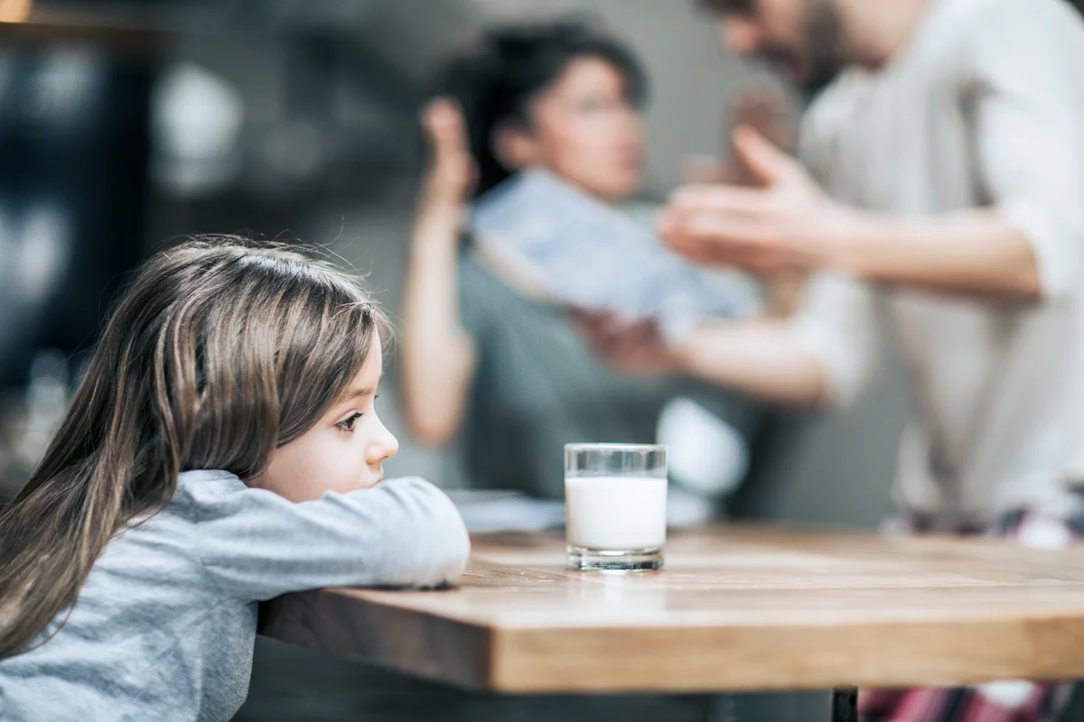 Little girl feeling sad while her parents are arguing in the background