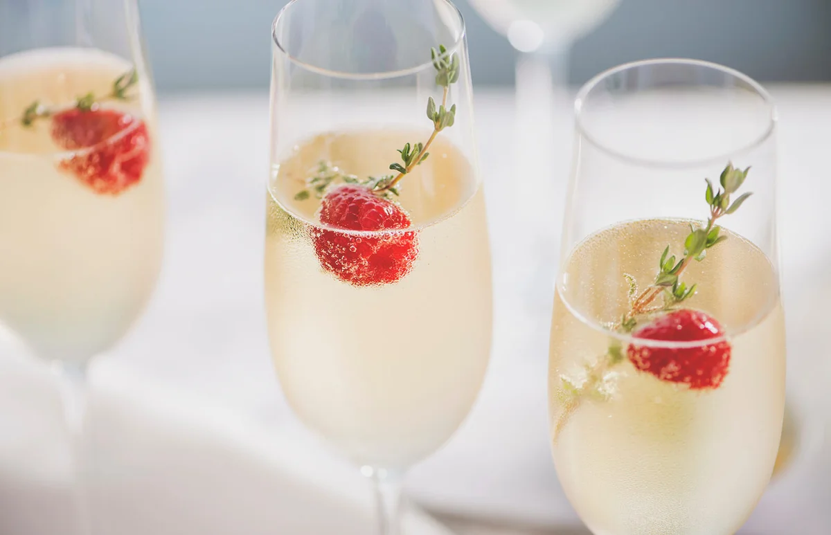Flutes of blanc champagne garnished with red raspberries