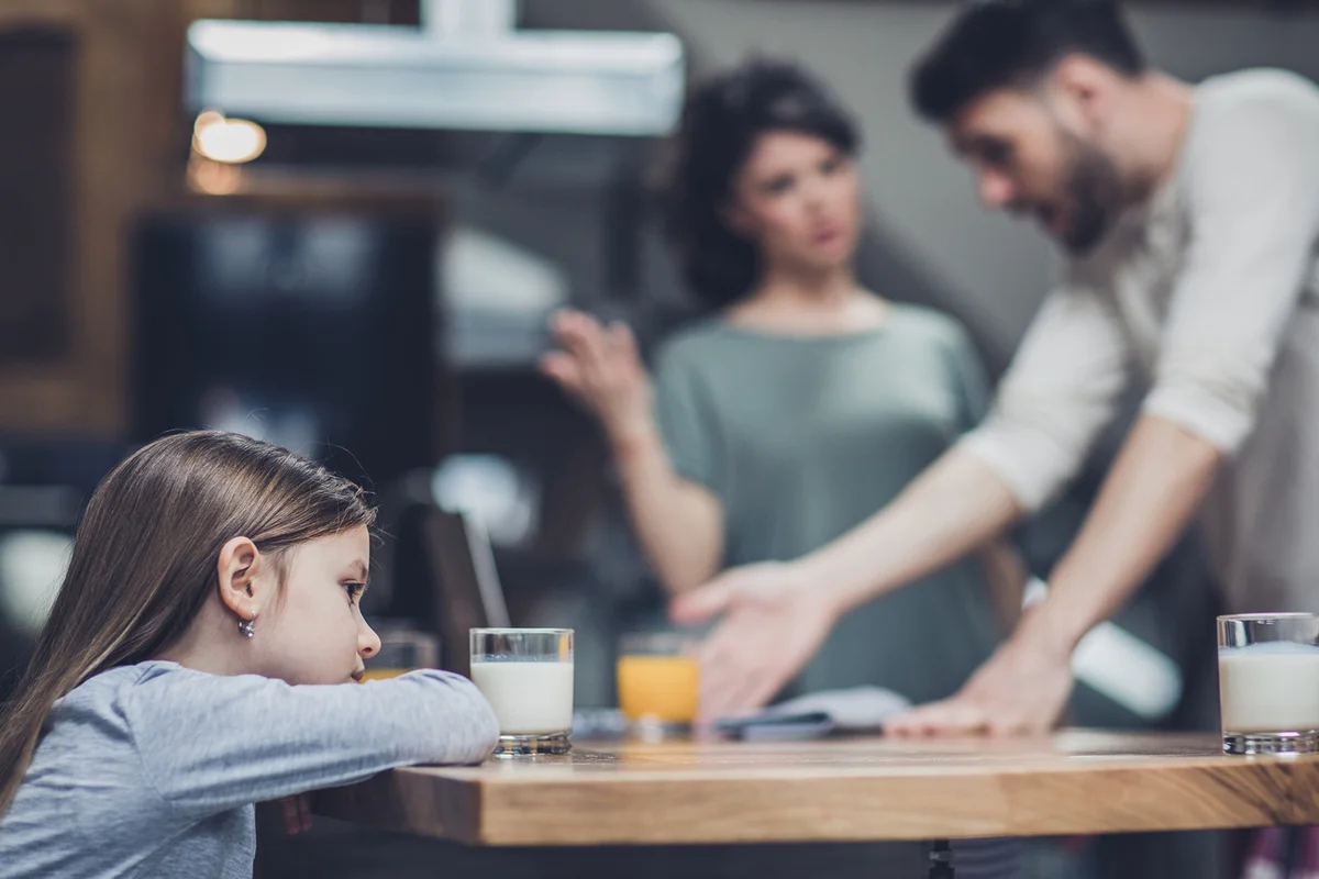 Little girl feeling sad while her parents are arguing in the background