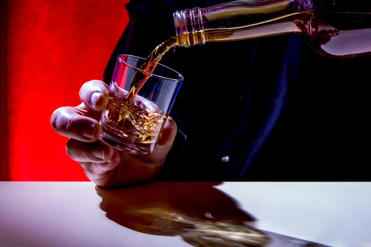 Man Pouring Whiskey In Glass At Table