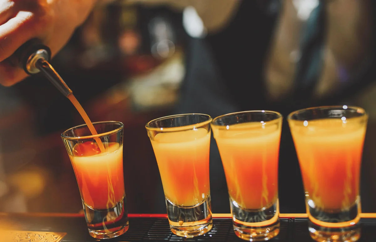 Bartender pouring shots with an orange alcoholic cocktail
