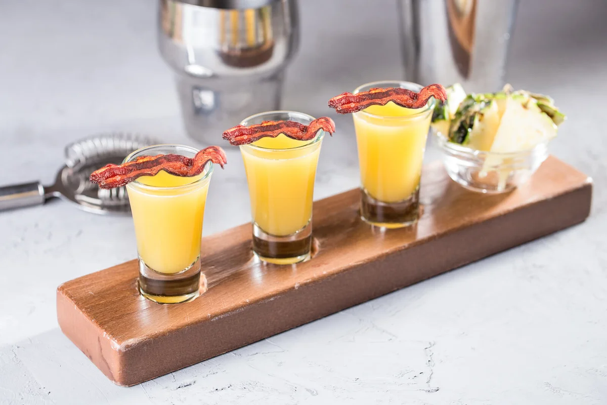 set of alcoholic cocktails in shot glasses with pineapple slices on wooden board