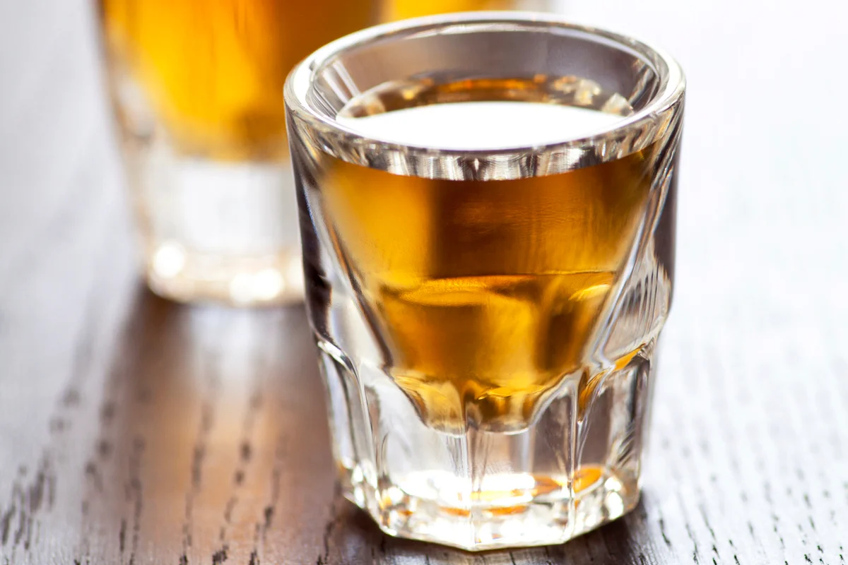 Three shot glasses full of whiskey on top of a bar table