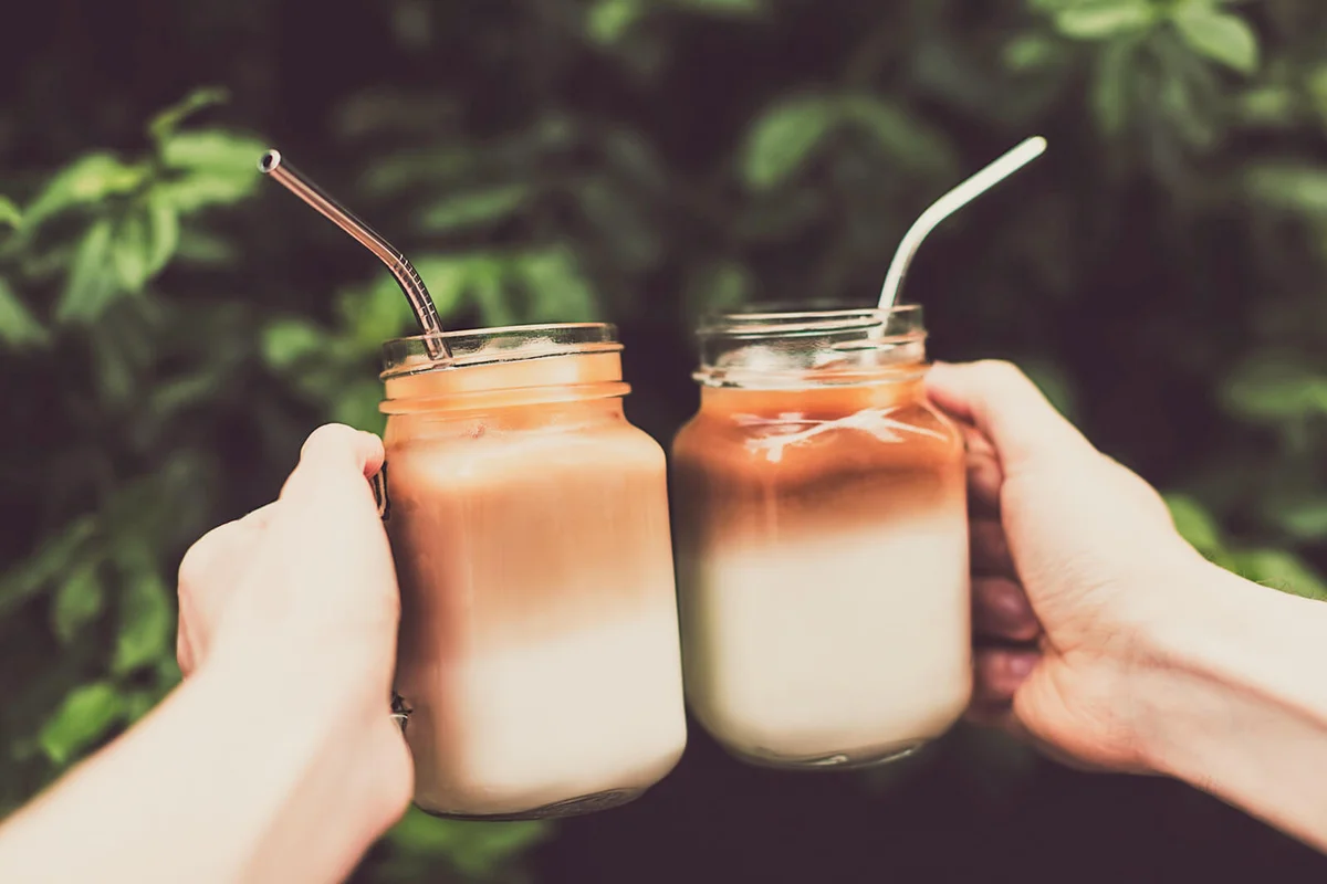 Two glass jars of ice coffee in woman and man hands