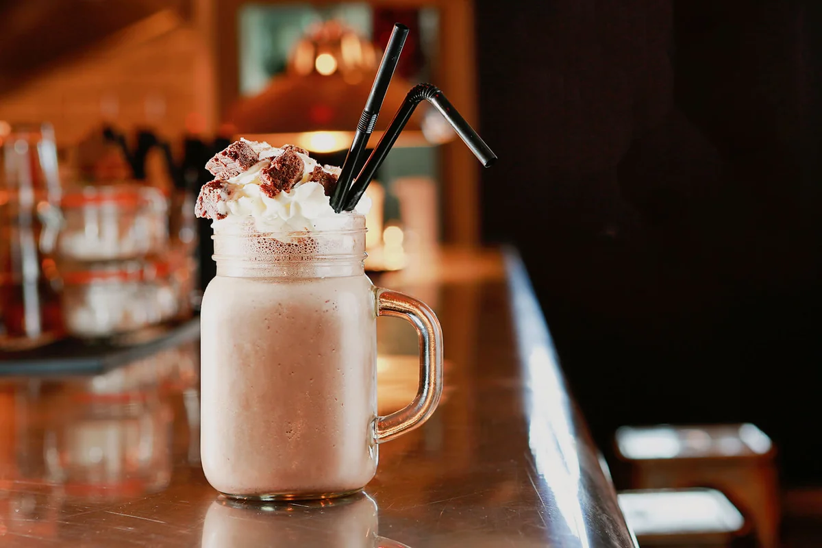 delicious and very tempting chocolate milkshake topped with cream and milk chocolate flake pieces