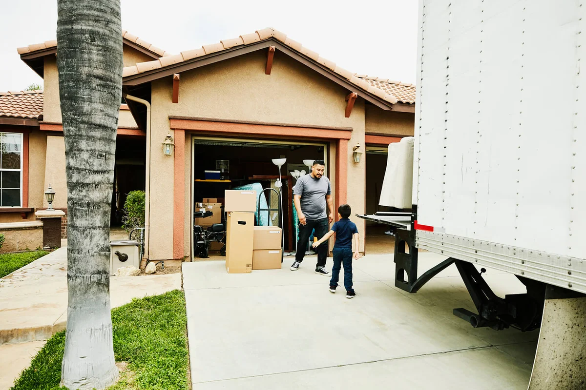 son helping father move items from moving truck into new house