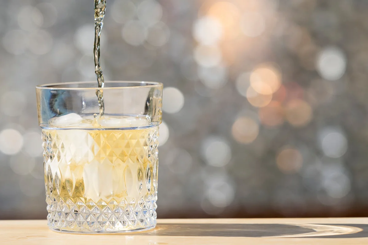 Bottle of whiskeys filling a glass with ice on the table of a bar outdoors