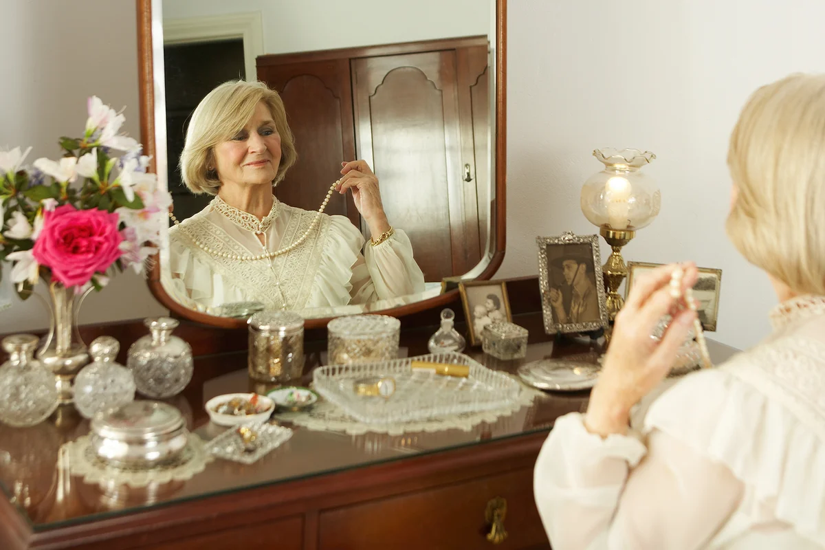 Senior woman sitting at vanity set, trying on necklace