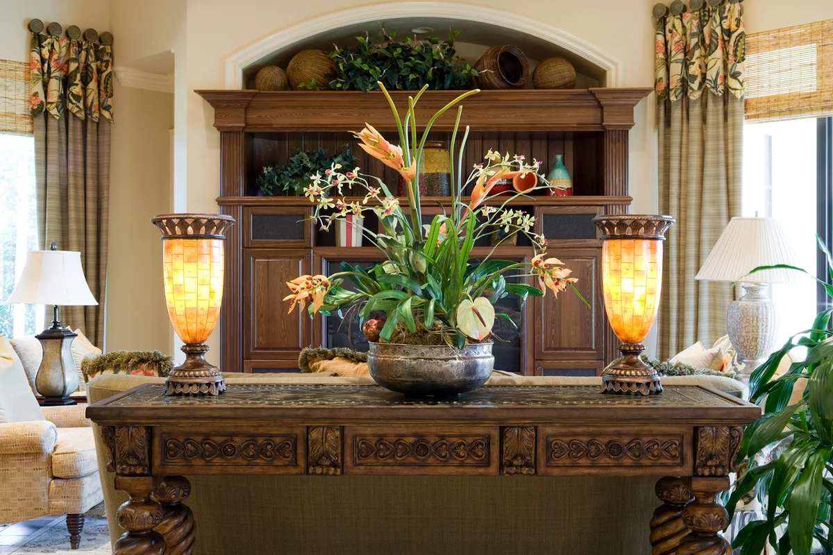 Beautiful carved console table with silk plant and lighted fixtures in a den