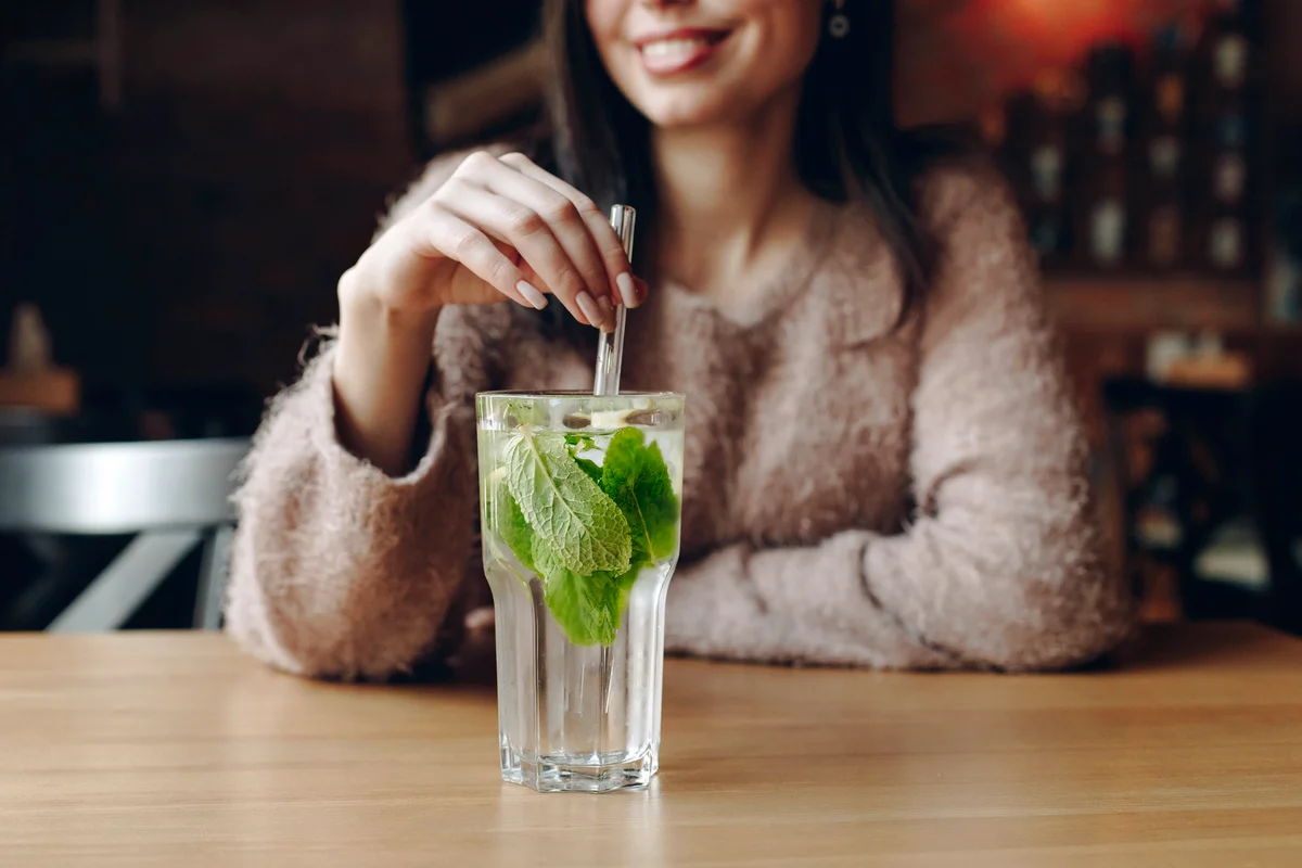 Woman holding straw in cocktail with mint leaves