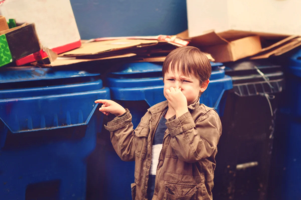 Boy standing by stinky dumpsters